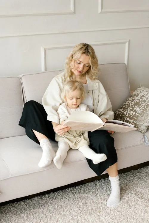 A mother reading a book with her young daughter on the sofa